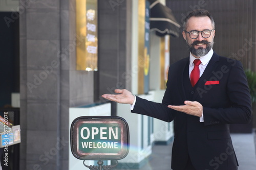 Caucasian waiter standing outside the luxury restaurant with open sign to welcome and greeting the customer	 photo