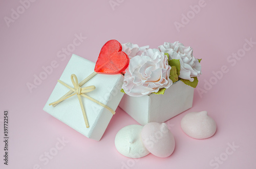 Gift box with flowers and meringues on a pink background.