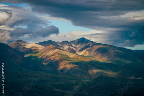 Awesome highland landscape with great mountains and blue clearance in cloudy sky in overcast weather. Blue skylight in cloudy sky above huge multicolor mountains in sunlight. Colorful mountain scenery © Daniil