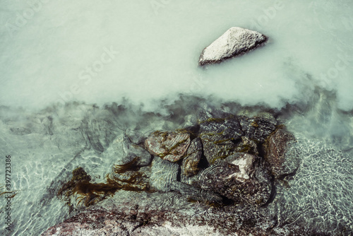 Nature background with mossy stones on silver water of mountain river. Silver sand on sandy bottom of mountain river. Shine on milky river surface. Gray nature backdrop with clear water with sand.