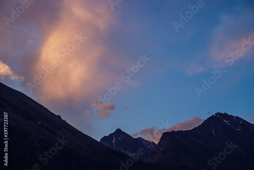 Amazing vivid landscape of sunset with silhouettes of rocky mountains and glow orange clouds. Atmospheric highland scenery with great mountain silhouettes under dawn sky. Glowing sunrise in mountains.