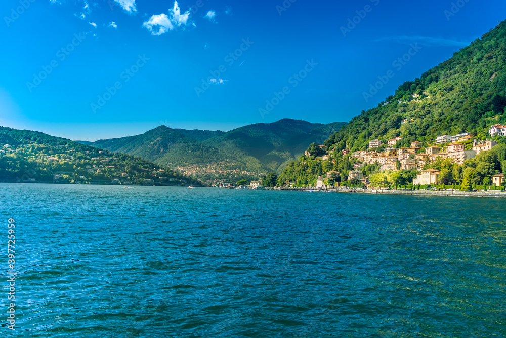Como Lake in city Como, Lombardy, Italy. Beautiful colorful landscape with mountains and lake water on sunny Summer day