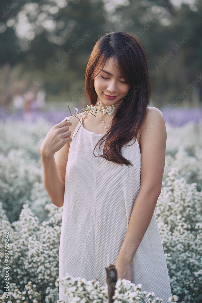 Shy Asian woman in white dress walking in the garden of white flowers
