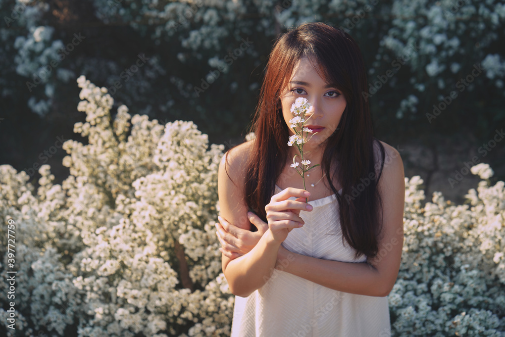 Asian woman in white dress covering her right eye by flower in the garden of white flowers