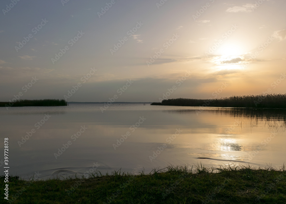 view of the lake before sunset, sunbeams through the clouds, calm water surface, lake meadow foreground