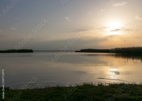 view of the lake before sunset, sunbeams through the clouds, calm water surface, lake meadow foreground