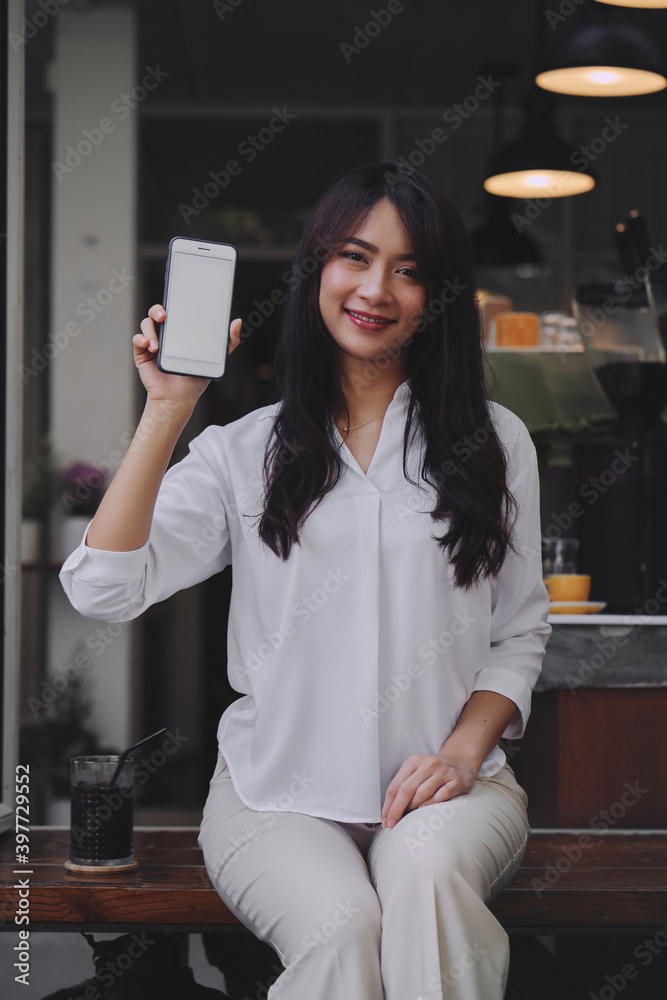 young attractive Asian woman showing her smartphone with white screen to the camera in a coffee shop mockup phone screen