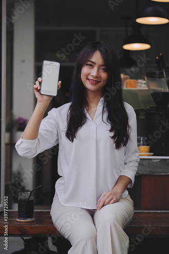 Obraz na płótnie young attractive Asian woman showing her smartphone with white screen to the camera in a coffee shop mockup phone screen w salonie