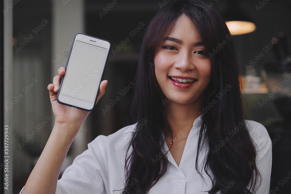young attractive Asian woman showing her smartphone with white screen to the camera in a coffee shop mockup phone screen