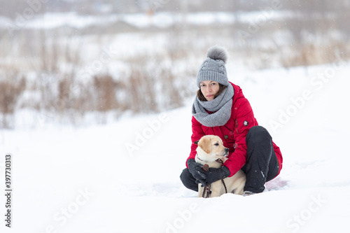 Young woman hugging Labrador puppy dog outdoor on snow in winter