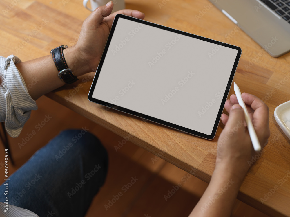 Male hand with stylus pen using digital tablet on wooden table