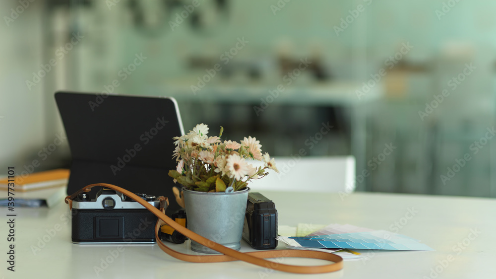 White table with camera, tablet, supplies and flower vase in office room