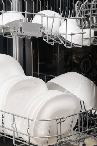 white plates and cups in the dishwasher compartment, close-up, side view
