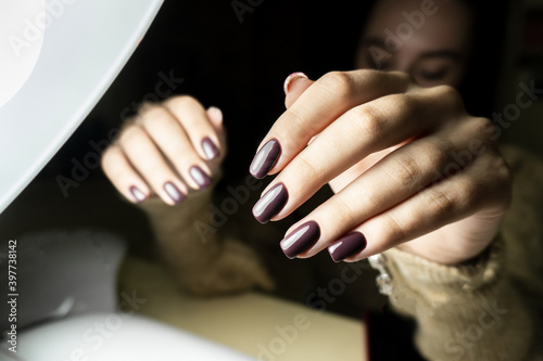 The girl shows a manicure after visiting a manicurist. The lamp shines on the nails. burgundy manicure