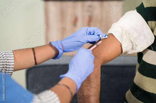 Close up of a Doctor making a vaccination shot in the shoulder of patient at home - concept of home health check.