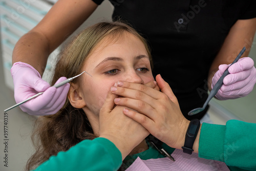 girl at the dentist's office closes her mouth with her hands