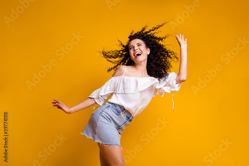 Profile photo of young cheerful funny curly brunette woman dancing wearing white top blue skirt isolated on vivid yellow colored background