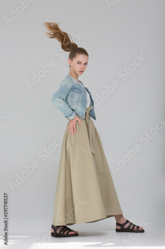 The model girl stands in a long skirt and blue jute. She takes a long stride, her hair in motion. Fashion look.