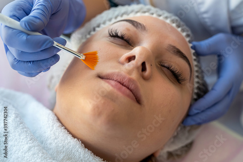 Cosmetologist applying healing cream on female client face skin in beauty clinic.