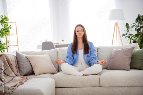 Portrait of pretty dreamy peaceful girl sitting on divan meditating free time in light flat house apartment indoor