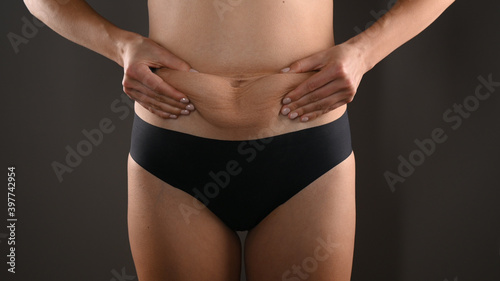 Woman in black panties squeezing fat at waist, close-up. Isolated on dark gray background © Tatsiana
