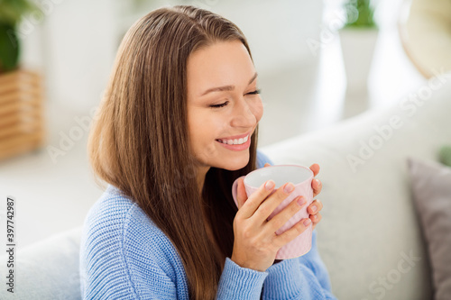 Close-up profile side view portrait of pretty cheerful dreamy girl sitting on divan drinking warm milk in light flat house apartment indoor