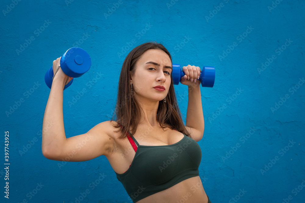 Athletic woman doing physical exercise using dumbbell over on blue background Athletic woman doing physical exercise using dumbbell over on blue background