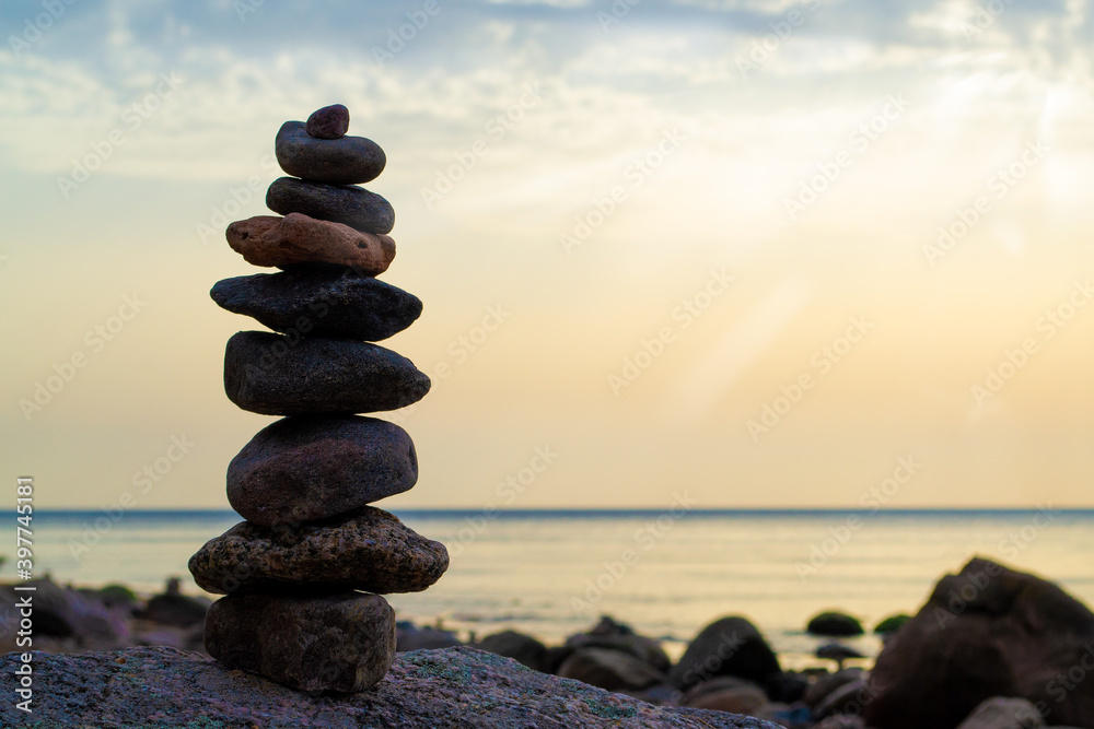 Fototapeta premium Pebble beach, beautiful view. Sun beams on sunrise and stones pyramid on the seashore. Rest and seaside vacation. Concept of balanced life, harmony and relax.