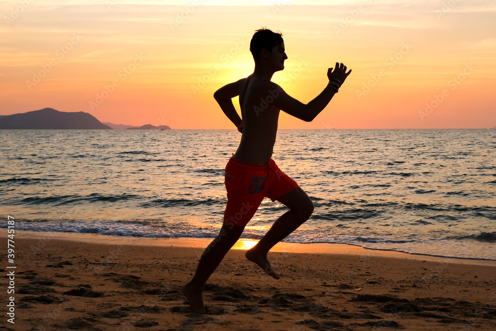 Silhouette of a young man running at the beach at sunrise with the sun in the background. Staying fit and healthy banner