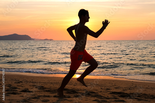 Silhouette of a young man running at the beach at sunrise with the sun in the background. Staying fit and healthy banner