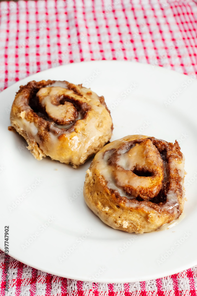 Hand made tasty cinnamon roll on a white plate and red and white table cloth. Pastry product. Hand made tasty cinnamon roll on a white plate and red and white table cloth. Pastry product.