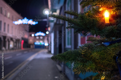 Night scene, candle on a fur tree in focus, town decorated and illuminated for Christmas out of focus. Festive season concept © mark_gusev