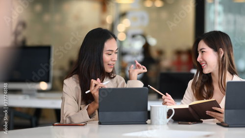 Two friendly businesswomen are discussing new ideas while working on computer tablet at office.v