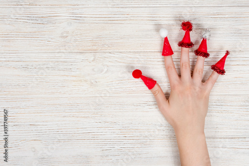 Female hand with red Christmas caps on fingers with hats with buboes on a wooden white background. Crezi new year. Place for an inscription. photo