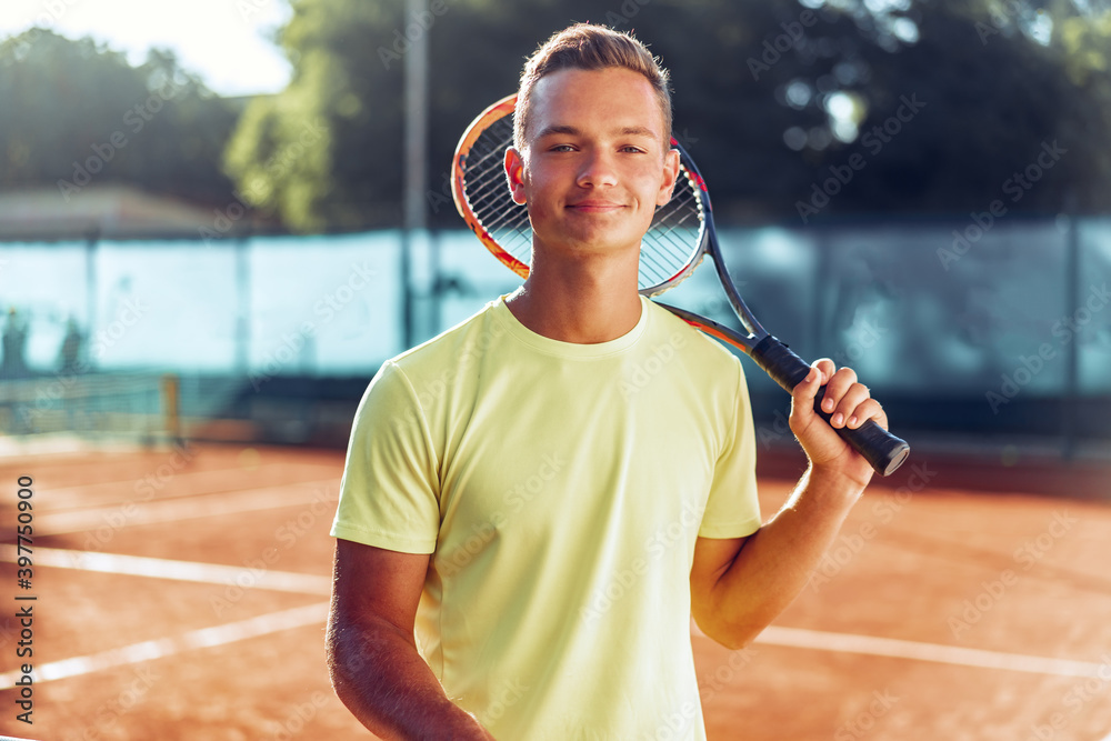 Young man teenager with tennis racket standing near net on clay court StockFoto Adobe Stock