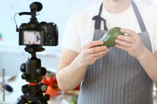 Man Vlogger Showing Ripe Tropical Avocado Fruit. Chef Holding Green Exotic Ingredient. Male Recording Culinary Recipe for Vlog on Camcorder. Healthy Vegetarian Food Partial View Photography.
