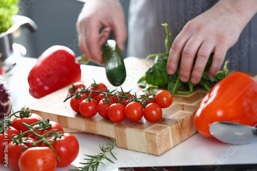 Male Hands Cooking Vegetables Kitchen Photography. Man Holding Green Cucumber and Sorrel. Small Red Cherry Tomato. Salad Vegetable on Wooden Cutting Board. Organic Ingredients Horizontal Photography