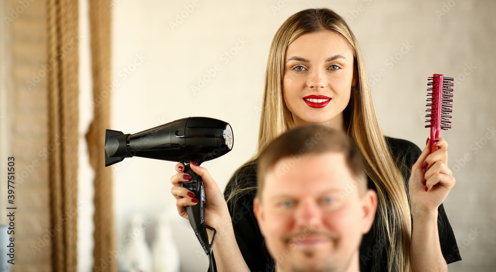 Blonde Hairstylist Using Dryer and Comb for Man.Young Hairdresser Styling Male Haircut with Hairdryer and Hairbrush. Woman Stylist Holding Tool for Hairstyling. Beautician and Client Looking at Camera Blonde Hairstylist Using Dryer and Comb for Man.Young Hairdresser Styling Male Haircut with Hairdryer and Hairbrush. Woman Stylist Holding Tool for Hairstyling. Beautician and Client Looking at Camera