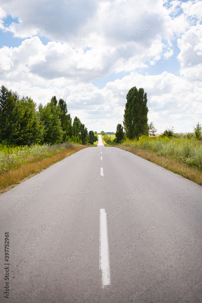 Asphalt flat road between rural fields. Summer, sunny day, beautiful sky