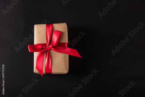 Black Friday Sale shopping concept, Top view of gift box wrapped brown paper and red bow ribbon present, studio shot on dark background