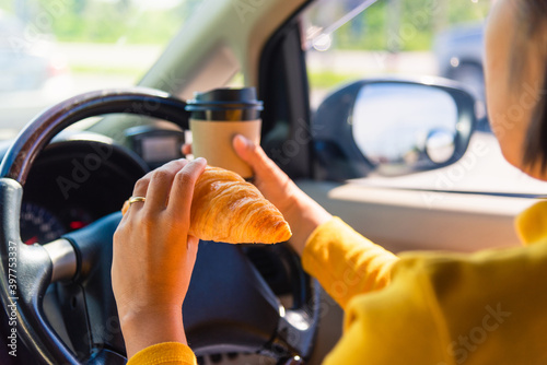 Asian woman eating food fastfood and drink coffee while driving the car in the morning during going to work on highway road, Transportation and vehicle concept photo