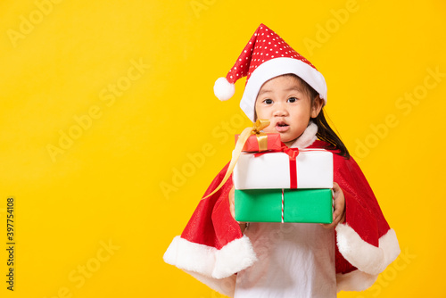 Asian little cute girl smile and excited, Kid dressed in red Santa Claus hat hold gift box on hands concept of holiday Christmas Xmas day or Happy new year, studio shot isolated on yellow background