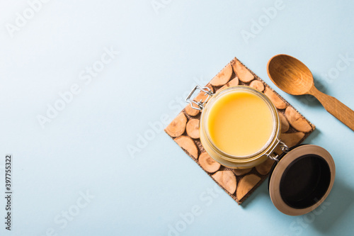 Ghee or clarified butter in jar and wooden spoon on blue background. Top view. Copyspace. Ghee butter have healthy fat and is a common cooking ingredient in many of the Indian food