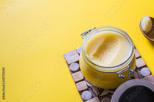 Ghee or clarified butter in jar and wooden spoon on yellow background. Top view. Copyspace. Ghee butter have healthy fat and is a common cooking ingredient in many of the Indian food