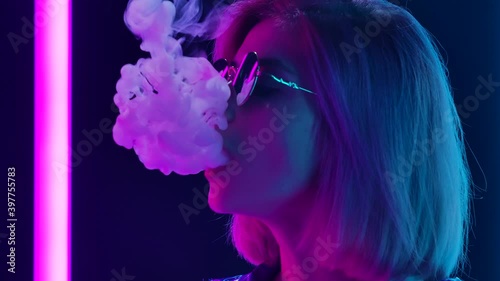 Portrait of a young stylish woman in sunglasses smoking a hookah and blowing out puffs of smoke. Close up. Slow motion.