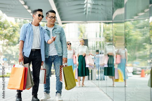 Handsome happy young Asian guys enjoying shopping together, thay are choosing sneakers in shop window