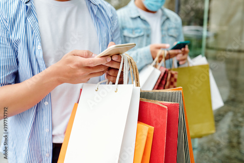 Close-up image of young people with shopping bags checking sales and offers via mobile applications