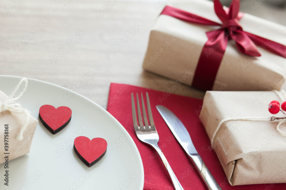 Festive table setting for Valentine's Day with plate, gift boxes, fork, knife and hearts on a wooden table. Festive table setting for Valentine's Day with plate, gift boxes, fork, knife and hearts on a wooden table.