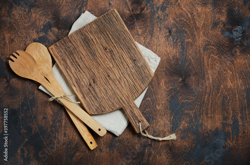 Wooden kitchen utensils. Wooden spoons, cutting board, napkin on a old wooden table. Top view.