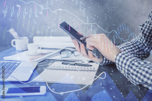 Double exposure of man's hands holding and using a digital device and forex graph drawing. Financial market concept.